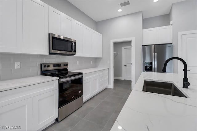 kitchen with appliances with stainless steel finishes, light stone counters, white cabinets, backsplash, and sink