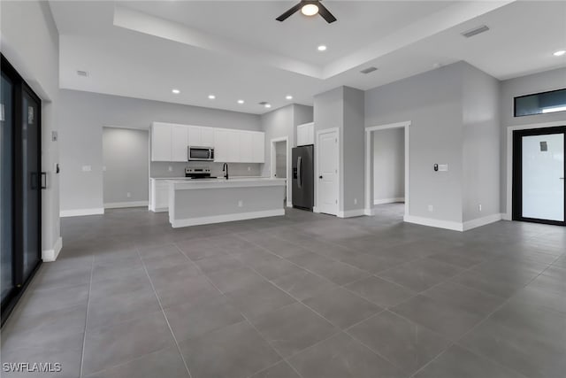 kitchen with ceiling fan, white cabinets, light tile patterned floors, a center island with sink, and stainless steel appliances