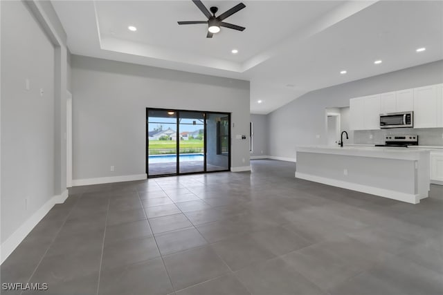 unfurnished living room with a raised ceiling, sink, and ceiling fan