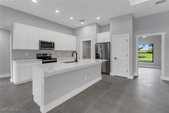 kitchen featuring light stone countertops, an island with sink, stainless steel appliances, and white cabinetry