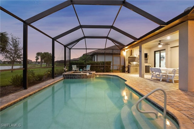 pool at dusk featuring glass enclosure, ceiling fan, exterior kitchen, an in ground hot tub, and a patio