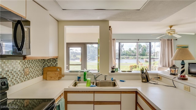 kitchen with decorative backsplash, white cabinets, ceiling fan, stove, and sink