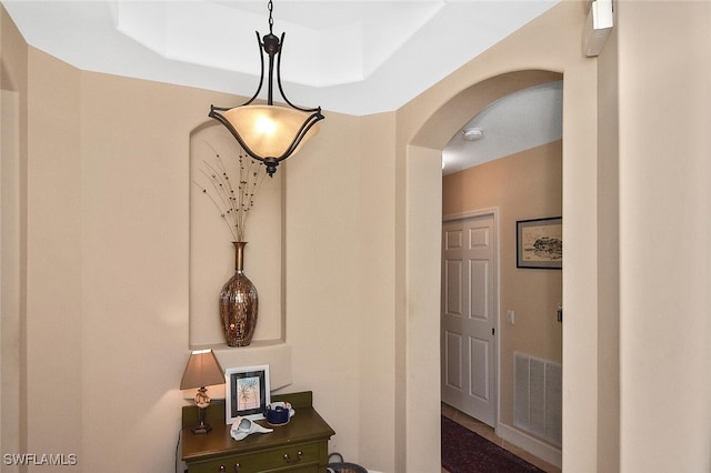 hallway with arched walkways, visible vents, and a raised ceiling