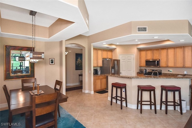 kitchen with a raised ceiling, pendant lighting, appliances with stainless steel finishes, a kitchen bar, and light tile patterned floors