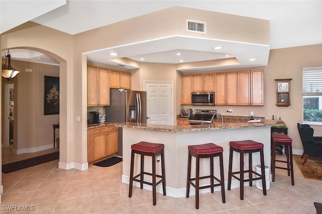 kitchen featuring light stone countertops, a breakfast bar, appliances with stainless steel finishes, a center island with sink, and light tile patterned floors