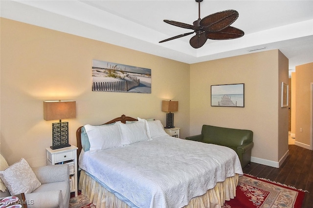 bedroom featuring visible vents, baseboards, a ceiling fan, a tray ceiling, and wood finished floors