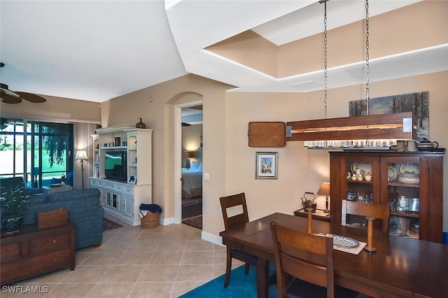 dining space with light tile patterned floors, baseboards, a ceiling fan, and arched walkways