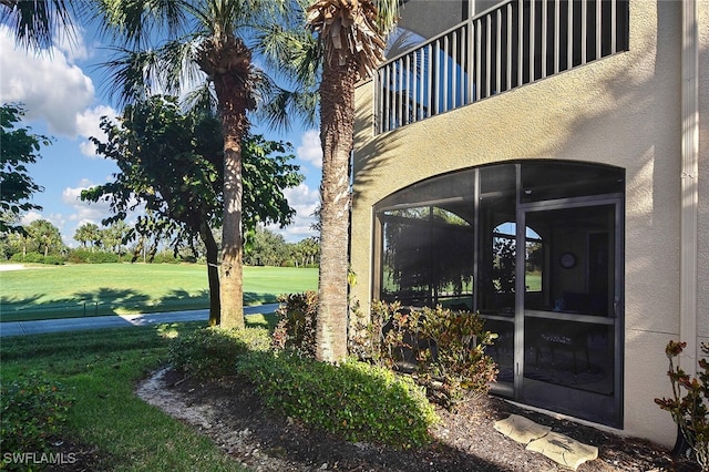 entrance to property with a yard, a balcony, and stucco siding