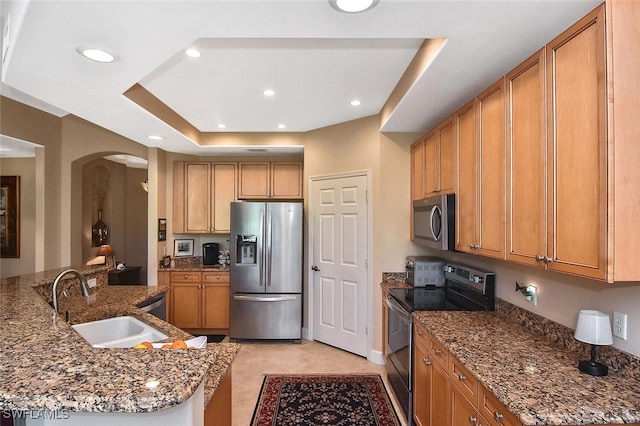 kitchen with light tile patterned floors, sink, appliances with stainless steel finishes, a tray ceiling, and dark stone countertops