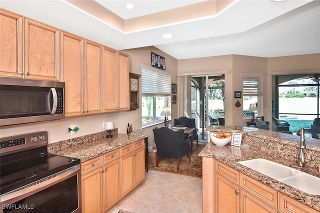 kitchen featuring light tile patterned floors, appliances with stainless steel finishes, light stone counters, a sink, and open floor plan