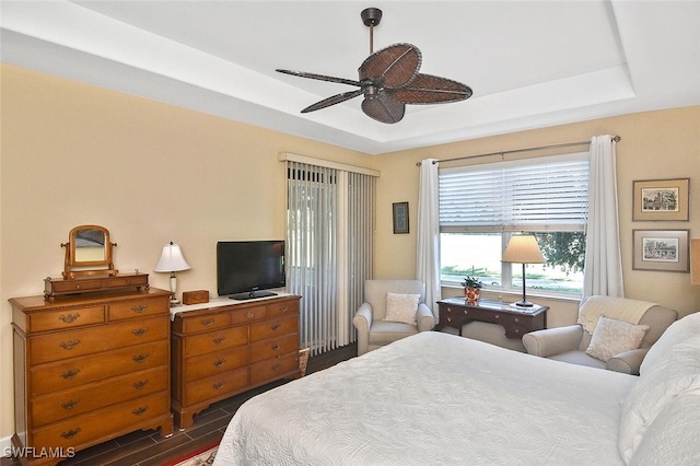 bedroom featuring ceiling fan, a raised ceiling, and dark wood-type flooring