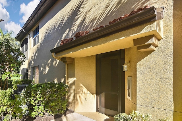 view of exterior entry with stucco siding and a tiled roof