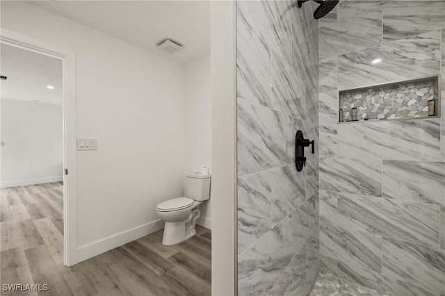 bathroom with tiled shower, wood-type flooring, and toilet