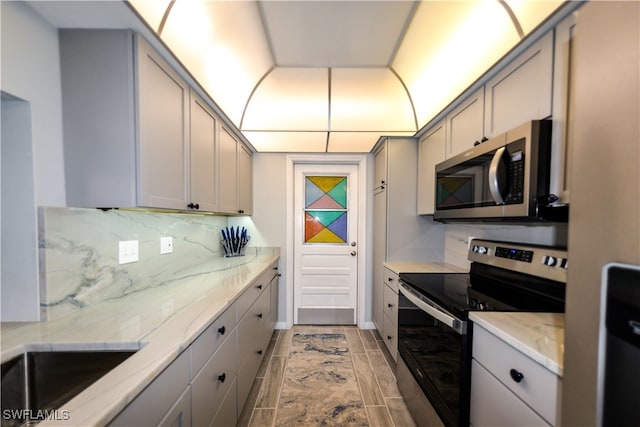 kitchen featuring decorative backsplash, light stone countertops, stainless steel appliances, and gray cabinetry