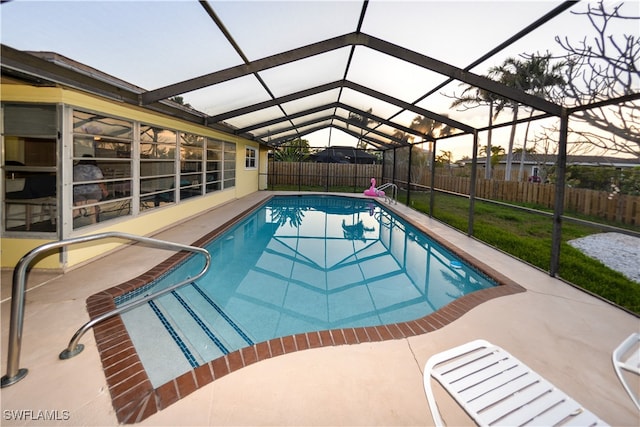 pool at dusk featuring a patio, a lawn, and glass enclosure