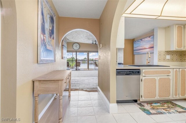 kitchen featuring light tile patterned floors, cream cabinets, sink, and stainless steel dishwasher