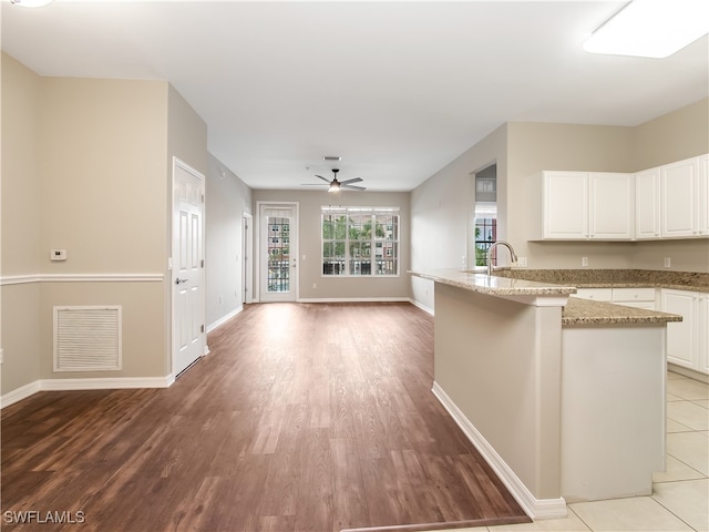 kitchen featuring ceiling fan, light hardwood / wood-style flooring, light stone counters, kitchen peninsula, and white cabinetry