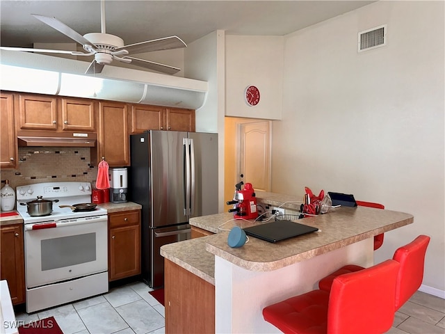 kitchen featuring a kitchen bar, electric stove, light tile patterned floors, tasteful backsplash, and stainless steel fridge