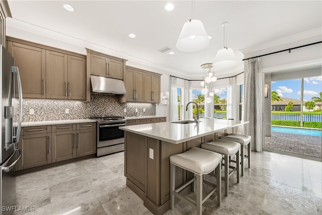 kitchen featuring decorative backsplash, an island with sink, stainless steel appliances, sink, and decorative light fixtures