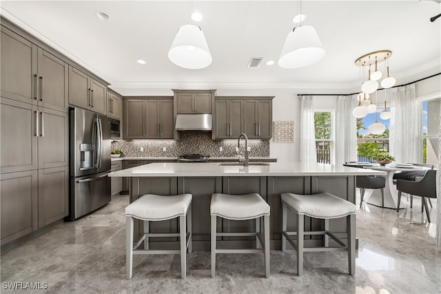 kitchen with sink, hanging light fixtures, stainless steel appliances, decorative backsplash, and a center island with sink