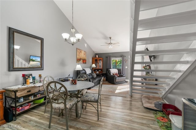 dining space with hardwood / wood-style flooring, ceiling fan with notable chandelier, and high vaulted ceiling