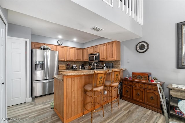 kitchen with a breakfast bar, kitchen peninsula, light hardwood / wood-style flooring, stainless steel appliances, and backsplash