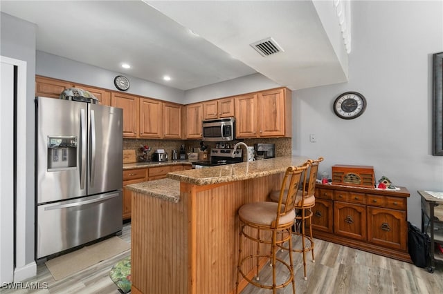 kitchen featuring tasteful backsplash, a breakfast bar area, kitchen peninsula, stainless steel appliances, and light stone countertops