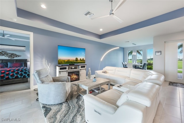 living room featuring ceiling fan, a fireplace, light tile patterned floors, and a tray ceiling