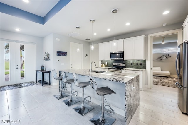 kitchen with a kitchen island with sink, sink, white cabinets, hanging light fixtures, and appliances with stainless steel finishes