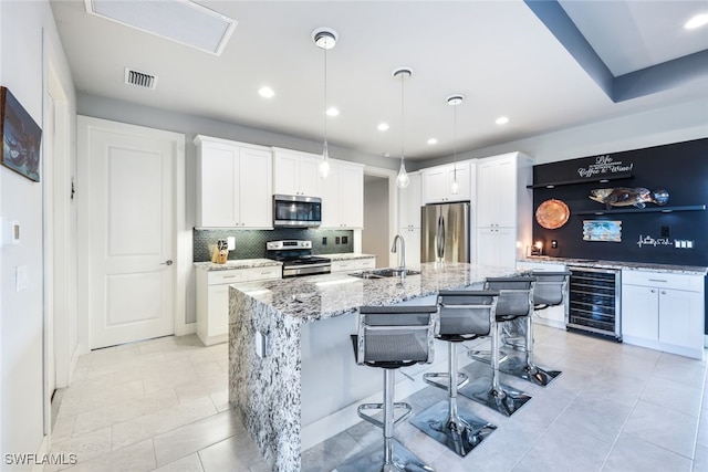 kitchen featuring pendant lighting, wine cooler, a kitchen island with sink, sink, and appliances with stainless steel finishes