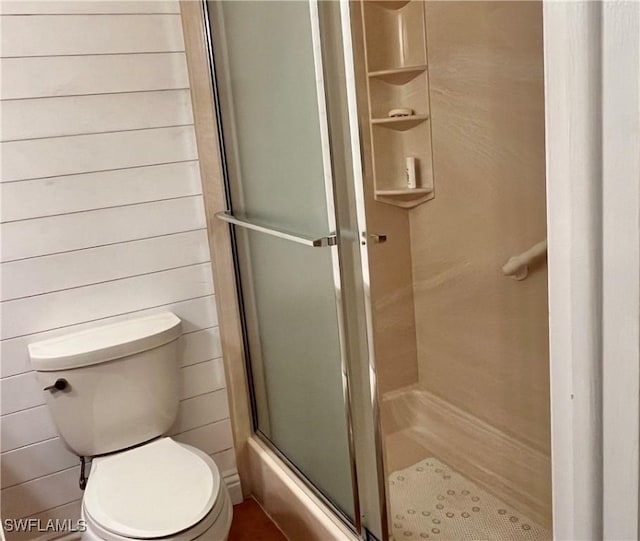 bathroom with toilet, a shower with shower door, and wooden walls