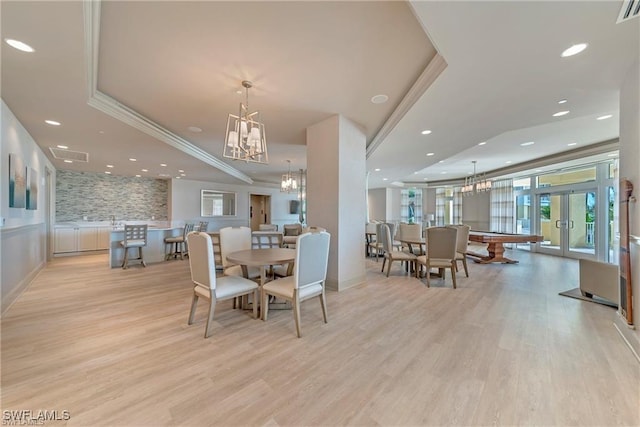 dining room featuring french doors, a tray ceiling, light wood-type flooring, and a notable chandelier