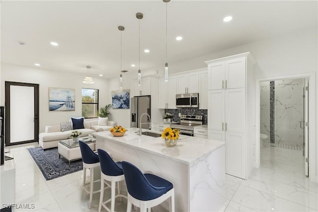 kitchen featuring light stone countertops, decorative light fixtures, a kitchen island with sink, white cabinets, and appliances with stainless steel finishes