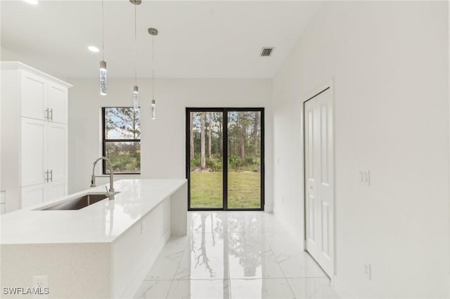 kitchen featuring a kitchen island with sink, sink, white cabinets, and decorative light fixtures