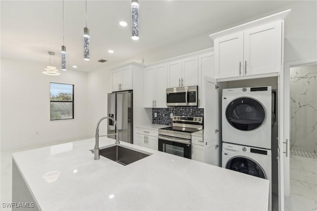 kitchen with stainless steel appliances, sink, decorative light fixtures, stacked washer and clothes dryer, and white cabinetry