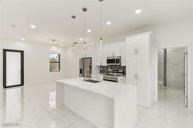 kitchen with white cabinets, appliances with stainless steel finishes, decorative light fixtures, and a kitchen island with sink