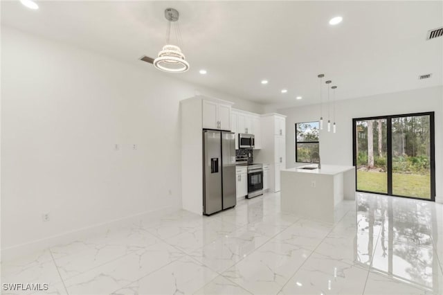 kitchen featuring appliances with stainless steel finishes, decorative light fixtures, white cabinetry, and a kitchen island