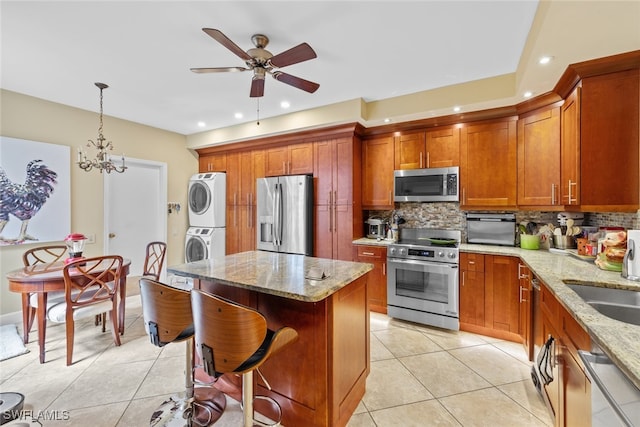 kitchen featuring decorative backsplash, stacked washer and clothes dryer, stainless steel appliances, decorative light fixtures, and light stone counters