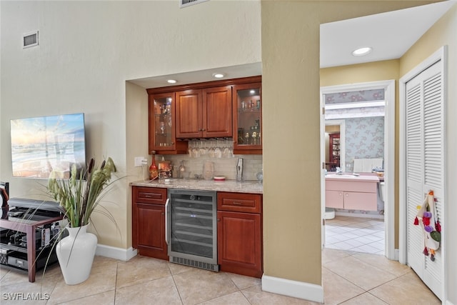 bar featuring backsplash, beverage cooler, sink, light stone countertops, and light tile patterned floors