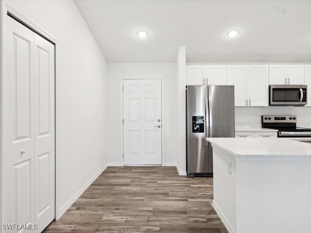 kitchen with appliances with stainless steel finishes, light hardwood / wood-style floors, light stone countertops, and white cabinets