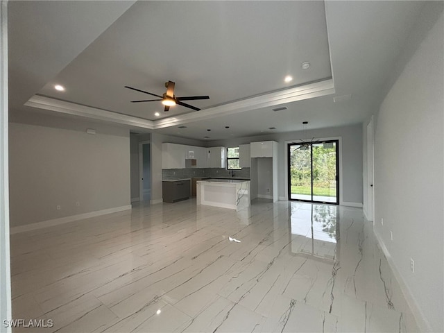 unfurnished living room featuring a raised ceiling and ceiling fan