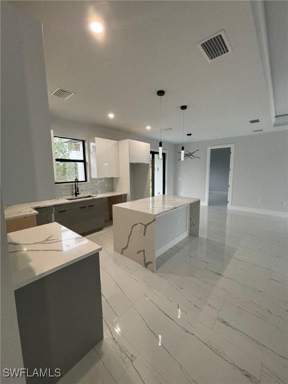 kitchen with backsplash, sink, pendant lighting, a center island, and white cabinetry