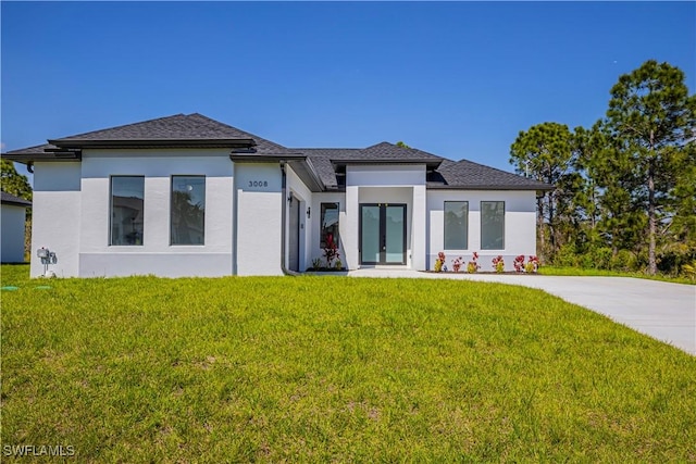 prairie-style home with french doors, a front lawn, roof with shingles, and stucco siding