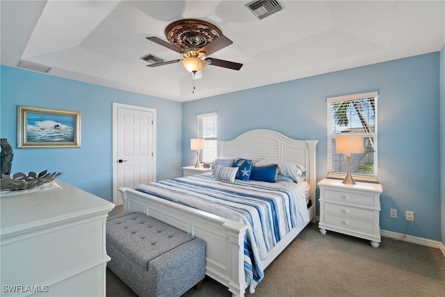 carpeted bedroom featuring ceiling fan, a tray ceiling, and multiple windows