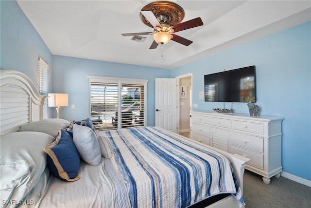 bedroom with a raised ceiling, dark carpet, and ceiling fan