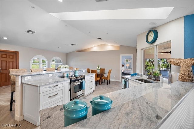 kitchen featuring appliances with stainless steel finishes, a kitchen breakfast bar, vaulted ceiling with skylight, white cabinets, and light stone counters