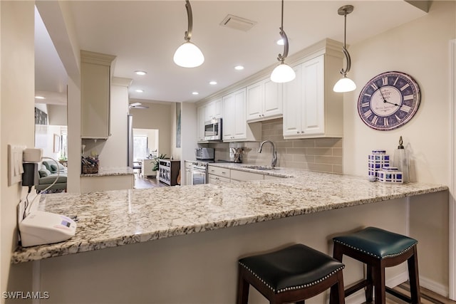 kitchen with kitchen peninsula, decorative backsplash, stainless steel appliances, sink, and decorative light fixtures