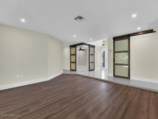 spare room with ceiling fan, a barn door, and dark hardwood / wood-style flooring