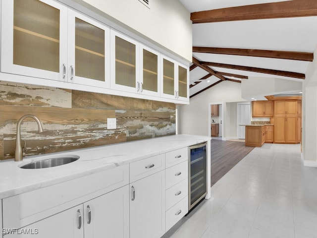 kitchen with sink, beverage cooler, white cabinetry, lofted ceiling with beams, and light stone countertops