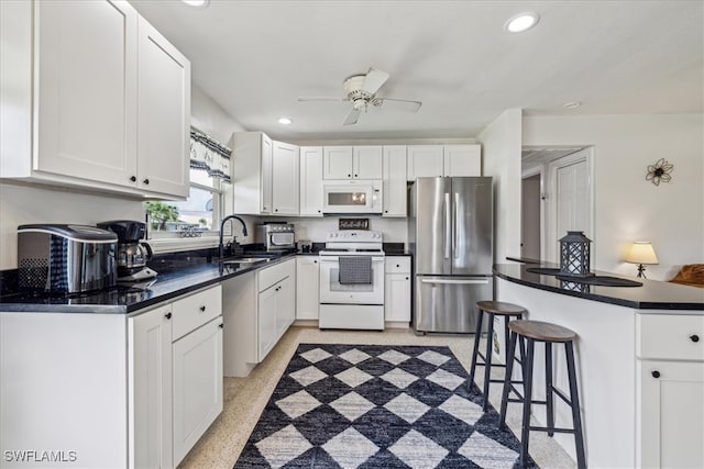 kitchen featuring white cabinets, white appliances, a breakfast bar area, ceiling fan, and sink